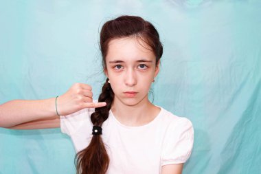 Uzun örgülü bir kız, J harfini elleriyle sağır ve dilsizlerin işaret dilini kullanarak gösteriyor. Orta plan, turkuaz arkaplan.