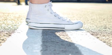 Beyaz spor ayakkabılı ayaklar asfaltta çift katlı bir çizgi üzerinde duruyor. Yakın çekim, seçici odaklanma.