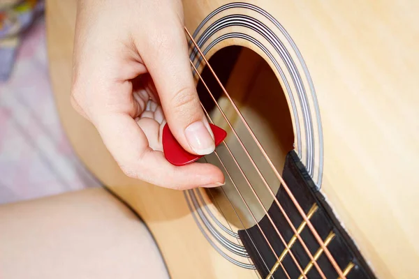 A woman\'s hand plays a guitar pick on the strings. Close-up, selective shot.