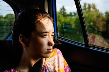 Düşüncelere dalmış genç bir kız gün batımında arabanın camından dışarı bakar. Yakın plan portre.