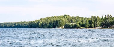 Gölün karşı kıyısında, kumsalın ağaçların arasında olduğu yerde. Seçici çekim, yatay çerçeve.