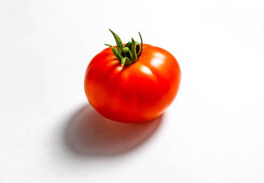 Beyaz arka planda açık bir gölgesi olan olgun kırmızı bir domates. Üst görünüm, seçici çekim.