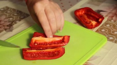 Bir kadın evdeki kesme tahtasında kırmızı dolma biber kesiyor. Yakın çekim, seçici odaklanma.