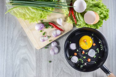 Tavada çiğ yumurta ve ahşap arka planda malzemeler. Tavada çiğ yumurta ve malzemeler.