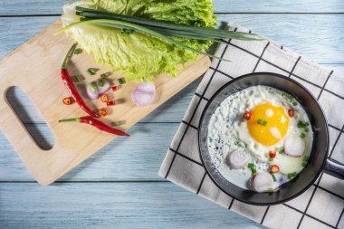 Tavada yumurta ve malzemeler mavi ahşap ve kumaşta.