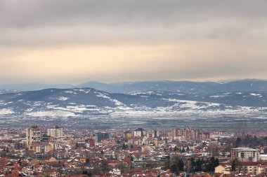 Sırbistan 'ın Pirot şehrinin güzel günbatımı manzarası, karla kaplı uzak ufuk dağlar ve karanlık, bulanık bulutların altında altın gökyüzü