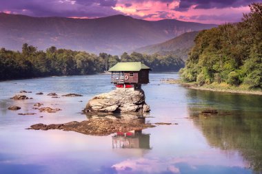 Drina evi dramatik günbatımı ve yansıması - Batı Sırbistan 'daki Drina nehrinin ortasındaki kayanın üzerindeki renkli küçük ev, bu bölgenin en popüler yerlerinden biri.