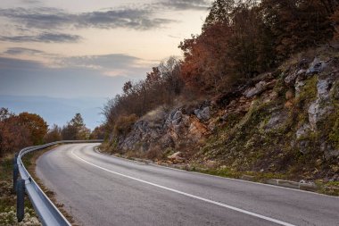 Beyaz çizgili kıvrımlı dağ yolu, sonbahar renkleri ve güzel gün batımı gökyüzü ve güneşli kayalar.