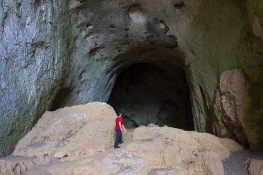 Sırbistan 'daki Eski Dağ' da Vladikine 'in etkileyici mağarasının devasa, etkileyici girişinde kırmızı gömlekli adam dikiliyor