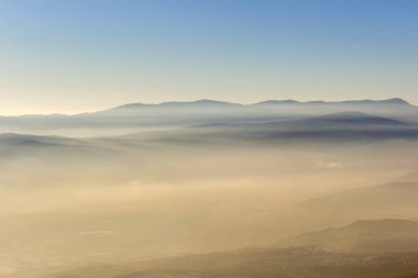 Yumuşak, renkli, sisli dağ katmanları ve gün batımında altın sisle kaplanmış alanlar.