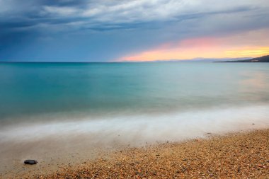Renkli gün batımı ve karanlık, fırtınalı bulutlar Neos Marmaras 'taki Paradisos sahilinin ipeksi deniz suyu üzerinde.