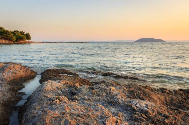 Neos Marmaras 'taki Paradaisos sahilindeki resiften gün batımında Yunanistan' daki Turtle adasının önündeki kayalar ve dalgalı deniz manzarası