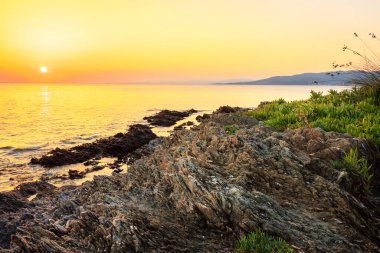 Yansıtıcı deniz suyundaki aşınmış kaya tabakaları ve Neos Marmaras 'taki Paradaisos sahilinin yakınlarındaki bir resifte batan güneş.
