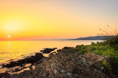 Yansıtıcı deniz suyundaki aşınmış kaya tabakaları ve Neos Marmaras 'taki Paradaisos sahilinin yakınlarındaki bir resifte batan güneş.