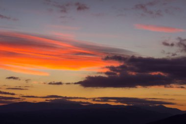 Gün batımı gökyüzünün, bulutların ve uzak ufuk dağlarının inanılmaz canlı renkleri.