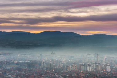 Gerçek dışı, mor gün batımı gökyüzü gece şehir manzarası şehir ışıkları kalın sisle kaplı.