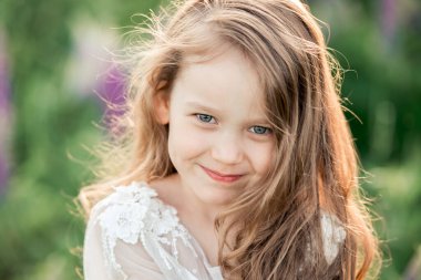 Gülümseyen yeşil gözlerin güzel portresi. Beyaz elbiseli, uzun kıvırcık saçlı beş yaşında bir kız. Dışarıda eğlen, yaz ve mutlu çocukluk kavramı.