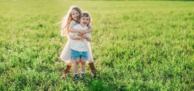 Şirin kıvırcık oğlan ve kız, gün batımında çayırda kalıyor, gülümsüyor ve sarılıyor. Sağlıklı, yaz tatili, arkadaşlık ve mutlu çocukluk kavramı.