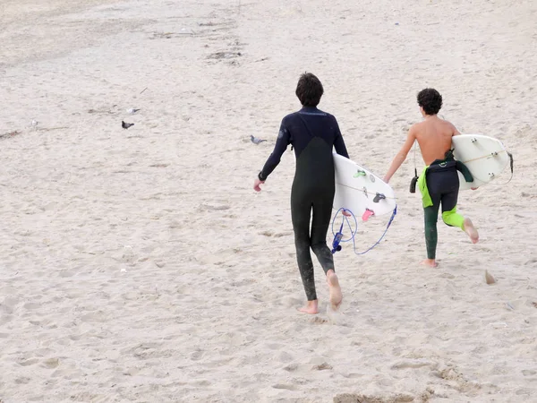 Серфингисты, несущие доску для серфинга на берегу океана — стоковое фото