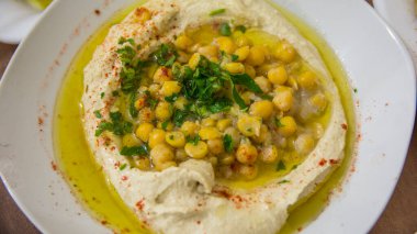Humus, geleneksel Orta Doğu Arap usulü nohut ezmesi, zeytin yağı, yeşil sebze ve baharatla beyaz bir kase içinde. Rameh, Kuzey Bölgesi, İsrail.
