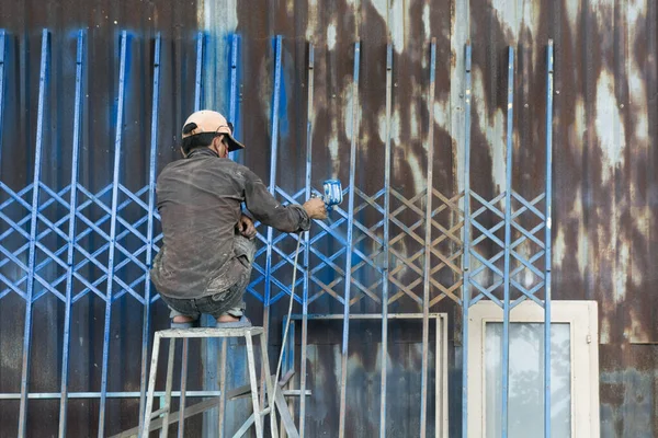 Vietnamese worker painting a fence in Blue, Hoi An, Vietnam