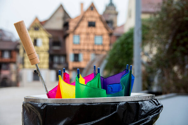 Broken colorful umbrella in garbage can, in front of colorful buildings, Colmar, Alsace, France.
