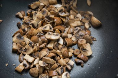 Tavada sotelenmiş mantar dilimlerinin (Agaricus bisporus) pişiriliş görüntüsünü kapat