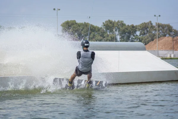 Man enjoying a Wakeboarding activity: a water sport in which the rider standing on a short board and pulled by a cables system in order to perform aerial maneuvers. Tel aviv, Israel