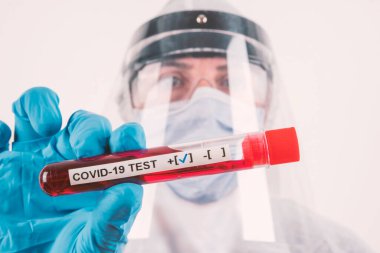 Corona virüs kan testi konsepti:: Maskeli bir laboratuvar bilimcisi, mavi tıbbi koruma eldivenleri ve POSITIVE COVID-19 sonuçlu bir test tüpü tutan gözlükler. Sığ alan derinliği