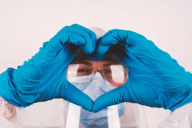 Corona virüsü salgını: Tıbbi hijyenik koruma gözlüğü ve mavi eldivenli bir kişi, sevgi ve birlikteliği ifade etmek için kalp şeklindeki parmaklarının arasından bakıyor