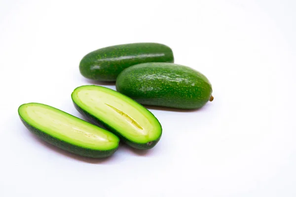 Beyaz arka planda üç mini avokado. Biri ikiye bölünmüş. Sağlıklı yaşam için özel ekilmiş egzotik yeşil vejetaryen yiyecekler.