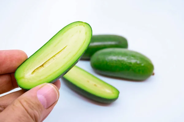 Beyaz arka planda üç mini avokado. Yarım dilimlenmiş bir avokadoyu tohum olmadan tutarken yaklaş. Sağlıklı yaşam için özel ekilmiş egzotik yeşil vejetaryen yiyeceği..