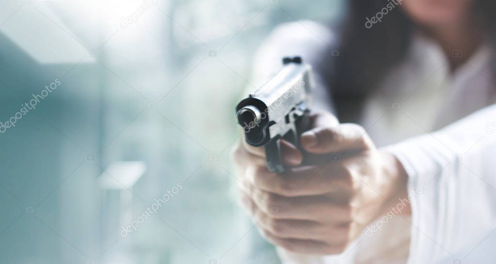 Woman pointing a gun at the target on blur background, criminal with gun, selective focus on front gun