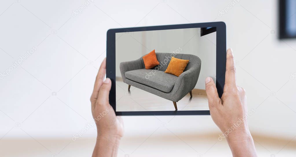 AR augmented reality. Hand holding digital tablet, AR application simulate sofa furniture and interior design  real room background