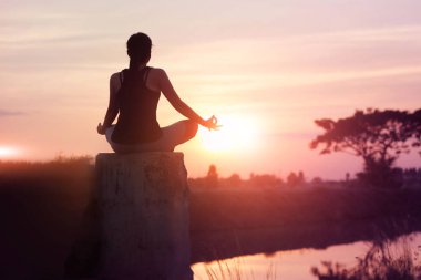 Kadın yoga uygulamaları ve doğa günbatımı arka plan üzerinde meditasyon.