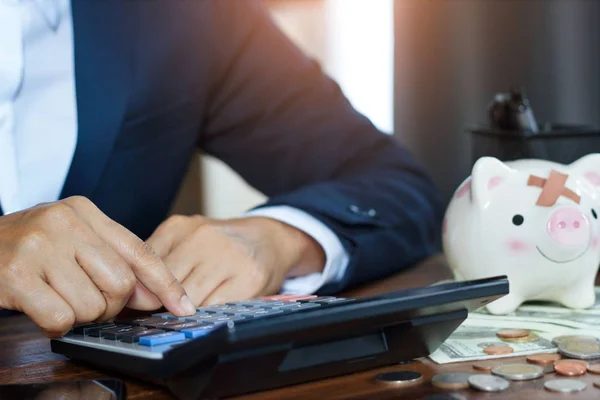 Businessman using calculator calculate of finances and piggy bank with money on table in office. business financing accounting banking Concept.