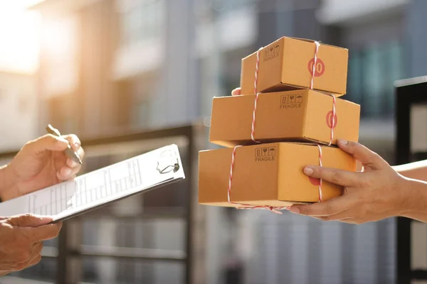 Uomo di consegna che tiene scatole di pacchi mentre un uomo firma documenti sullo sfondo del mattino — Foto Stock