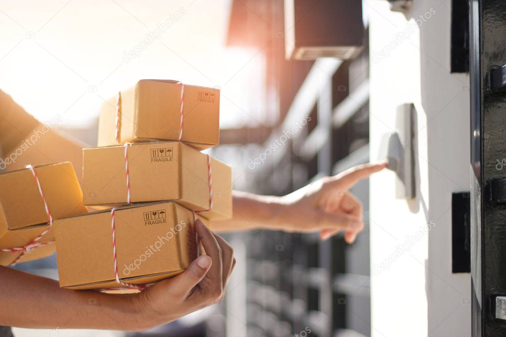 Delivery man holding parcel boxes and ring the doorbell on the client's door in the morning background.