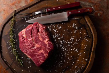 Ham Chuck Eye bifteğinin üst görüntüsü kaba tuz ve biberiyeyle tatlandırılmış, koyu ahşap desenli bir yüzey üzerinde, yazmak için alanı olan.