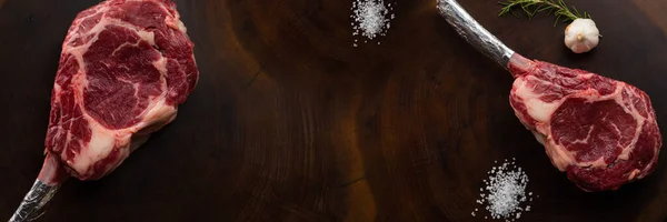 Baharat masajı, taze biberiye ve tuz ile ızgara malzemeli çiğ baltalı biftek, koyu ahşap dokusu ve yazmak için yeri olan bir masada.