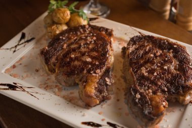 Küçük kızarmış patatesli ızgara sığır pirzolası. Dikdörtgen beyaz tabakta.