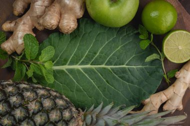 Yeşil detoks suyu, alttaki lahana yaprağı, zencefil, limon, nane, ananas ve yeşil elma hazırlamak için taze malzemelerin üst görünümü, kopyalama alanı