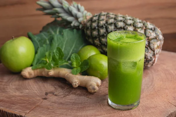 glass of juice and fresh ingredients for preparing detox green juice, kale leaf, ginger, lemon, mint, pineapple and green apple on wooden texture and with space for writing