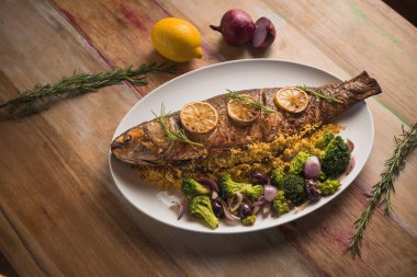 ahşap masada kızartılmış kefal, brokoli, soğan ve kurutulmuş portakal dilimleri.