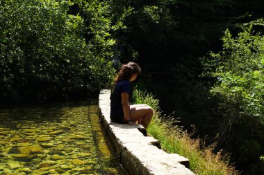 Genç bayan bir nehirle dağda oturuyor.