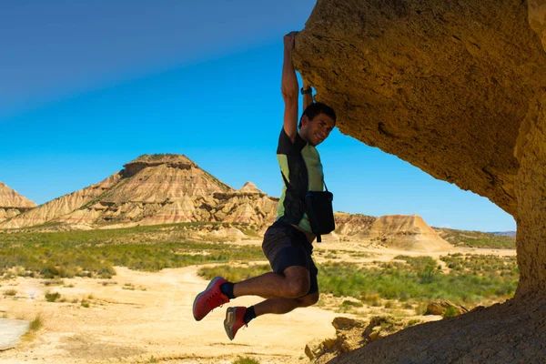 Genç adam bir kayada asılı duruyor.