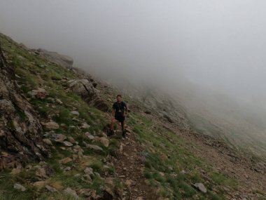 Genç adam pireneler içinde bir dağa tırmanıyor.