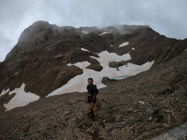 Genç adam pireneler içinde bir dağa tırmanıyor.