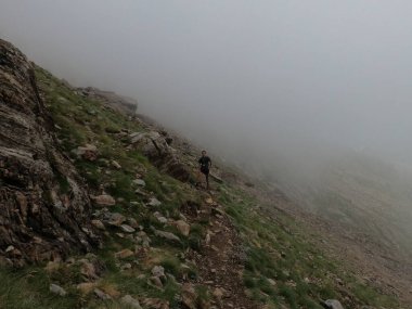 Genç adam pireneler içinde bir dağa tırmanıyor.