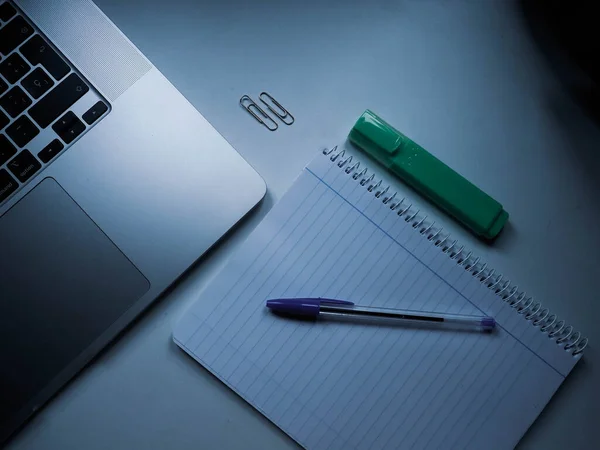 bir bilgisayar beyaz bir masada bir defter ve bir kalem.